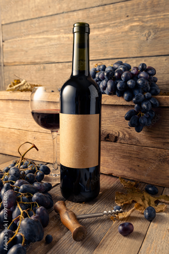 Fototapeta premium Bottle of red wine and blue grapes on a old wooden table.