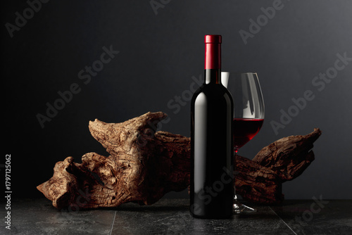 Red wine and old weathered snag on a black stone table.