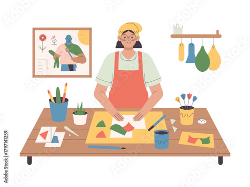 A woman crafting with paper shapes at a table, surrounded by art supplies and a framed picture, showcasing a creative and colorful scene