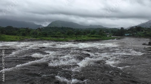 Monsoon Water Stream Rushing Over Rocky Terrain Amid Dramatic Clouds and Mountain Views
