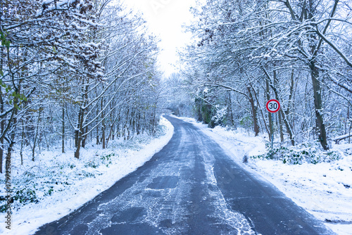 Asphalt road covered with ice among snowy forest. Road sign speed limit 