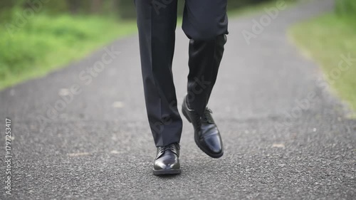 Wallpaper Mural Close-up of a man's legs in black trousers and leather shoes walking on an asphalt road. This scene evokes a sense of journey and purpose. Perfect for business or career concepts. Torontodigital.ca
