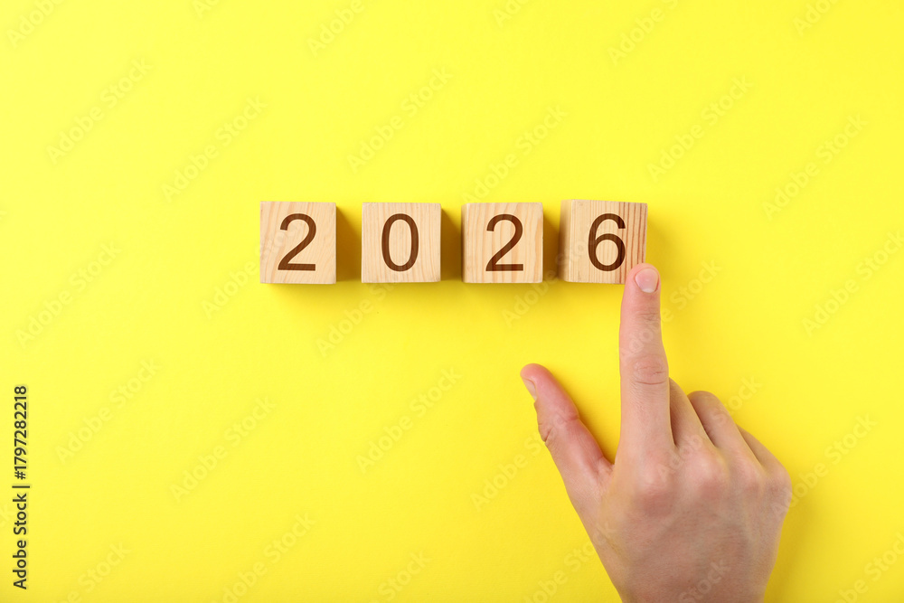 Fototapeta premium New 2026 year. Man putting cube with number 6 on yellow background, top view