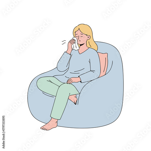 A sad young woman sitting on a bean bag chair, wiping tears with a tissue, feeling emotional distress.