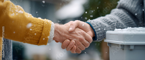 Close-up of two people shaking hands outdoors in winter with snow falling and wearing warm sweaters