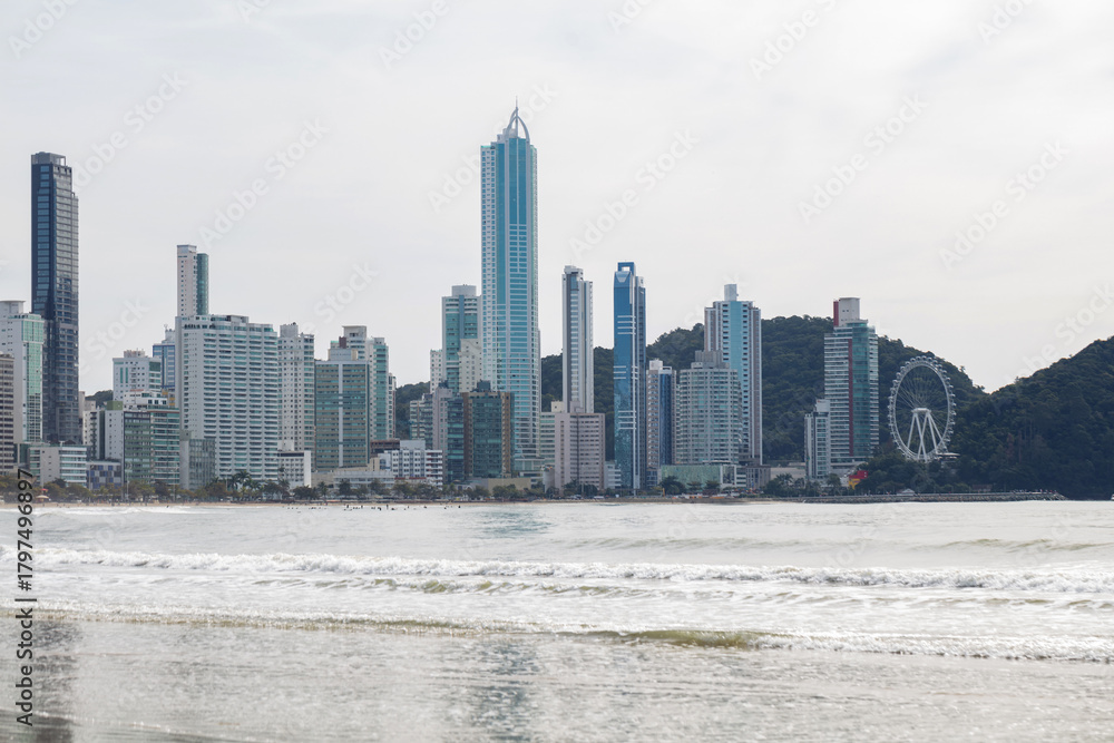 Fototapeta premium Beach with white sand and trees and buildings in the background in Balneario Camboriu, Santa Catarina, Brazil.