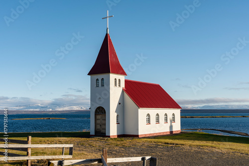 Quaint church stands serene against a backdrop of distant mountains and water.