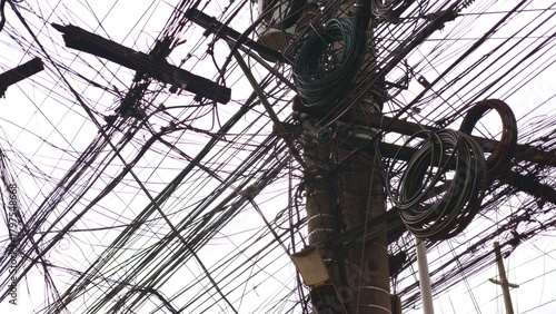Messy wiring clings to utility pole with hooks, wiring tangled in patterns, wiring representing overloaded systems. Close-up chaos and metal attachments. Designed for electrical safety campaigns.