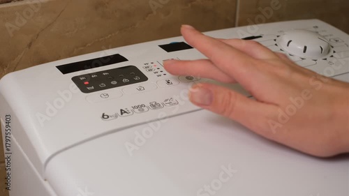 Woman selecting washing program on washing machine close-up of hands