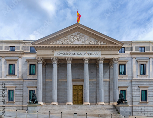 The neoclassical facade of the Spanish Congress of Deputies features six columns, a pediment, steps, and two large bronze lion statues flanking the main golden doorway