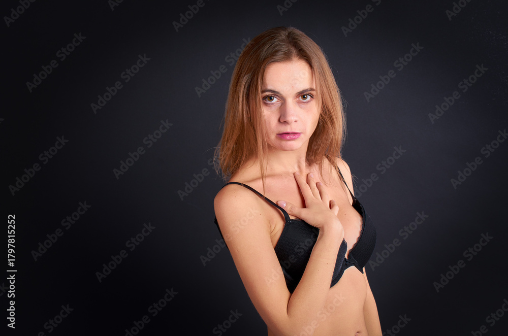 Fototapeta premium AIn the studio, against a black background, stands a beautiful and seductive girl in stockings and panties.