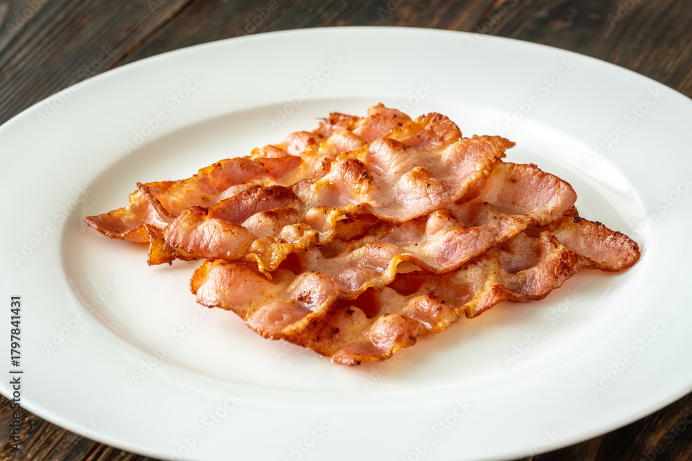 Naklejka premium Crispy fried bacon slices neatly arranged on simple white serving plate