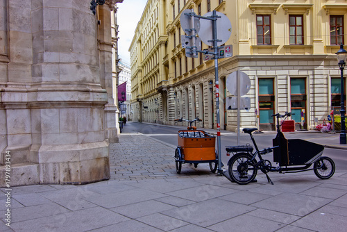 quiet, narrow street in Vienna, lined with historic yellow buildings, showing two cargo bikes