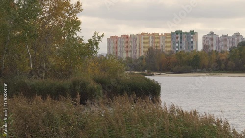 Urban Contrast in Kyiv: Tall residential buildings visible over the water, framed by reeds and autumn trees