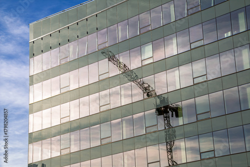 Construction crane reflection in the windows of office building against blue sky