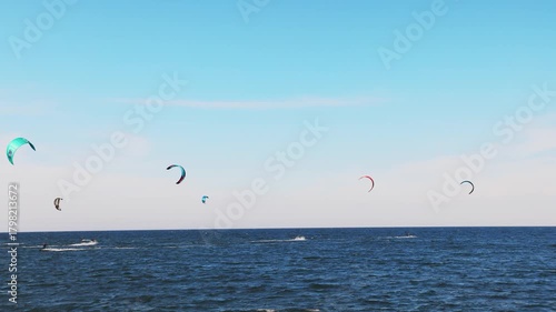 People in sportswear go kiting on the surface of the Black Sea near the town of Pomorie under a blue sky