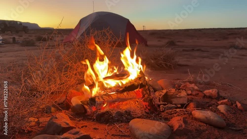 Campfire burning brightly at sunset beside a desert tent