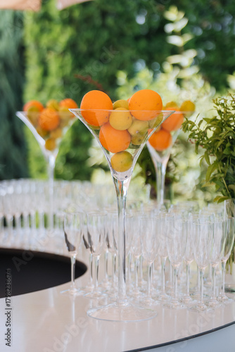 Tall martini centerpiece with citrus above rows of champagne flutes at an outdoor bar