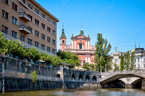 Fototapeta Naklejka Na Ścianę i Meble -  Ljubljana, Slovenia – July 14, 2025: A scenic view of the Ljubljanica River as it winds through the historic center of Ljubljana. Lined with trees, cafés, and charming riverside architecture.
