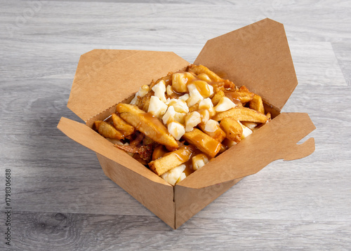 A cardboard takeout container of poutine French fries with cheese curds and gravy isolated