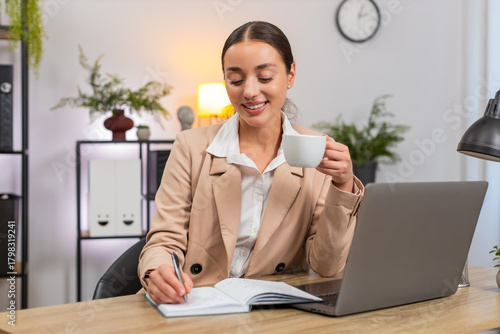 Картината върху платно Young businesswoman at home office drinks coffee slowly reads plan in notebook and sets priority list