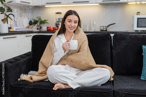 Free Download Young woman at home drinks tea wrapped in blanket relax calm breath gentle pause comfort. Caucasian girl on sofa holds cup slow sip eyes closed cozy rest soft smile warm mood quiet evening style vibe. - GFXLoad