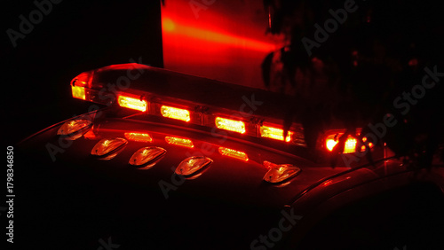 Red lights are shown while flashing on top of an ambulance at the scene of an emergency at night, shown up close while parked on a city street in the USA.