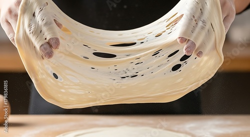 Professional baker's hands stretching a delicate, transparent sheet of pastry dough