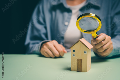 Hand examining wooden house with magnifying glass, property inspection awareness, investment analysis, financial planning clarity, budgeting insight, real estate evaluation concept