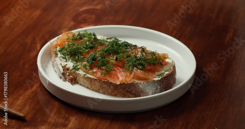 Top view on Sandwich with red fish. The chef rotation the plate in camera on which lies a salmon sandwich sprinkled with fresh dill, preparing a homemade appetizer.