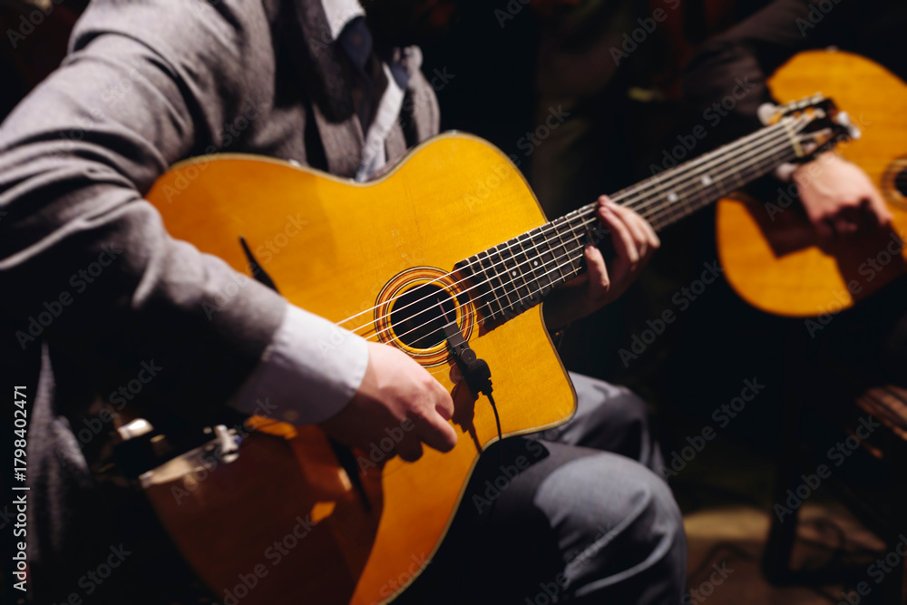 Obraz premium Concert view of acoustic electric guitar player with vocalist and rock band performing in a club, male musician guitarist on stage with audience in a crowded concert club hall arena, hands on guitar