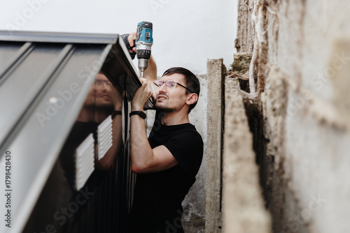 A young guy with a drill is installing a roof on a metal barn.