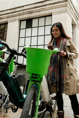 Woman using smartphone for e-bike rental in city