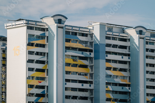 A colorful HDB block in Singapore with a distinctive geometric design. The building features a mix of white, yellow, and blue, with a prominent 