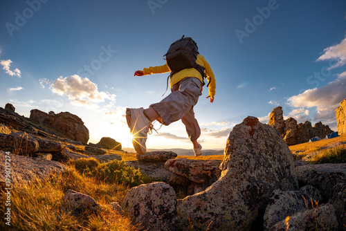 Female hiker woman girl jumps or make big step from rock to rock at sunset mountain top. Active vacations concept