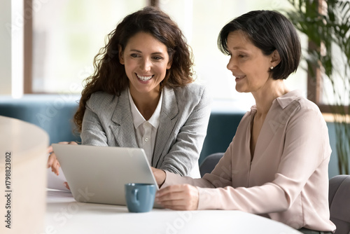 Young mature female professionals collaborating at notebook in friendly partnership