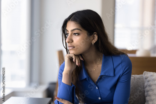 Thoughtful bored depressed young Indian woman leaning chin on hand