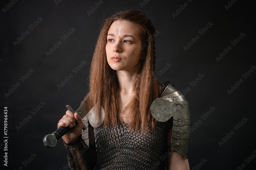 Naklejka premium Portrait of a young woman, fantasy warrior in armor with a sword in her hands isolated on a dark background