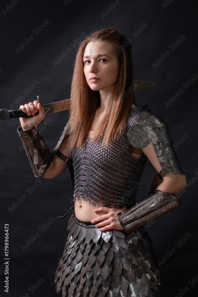 Naklejka premium Portrait of a young woman, fantasy warrior in armor with a sword in her hands isolated on a dark background