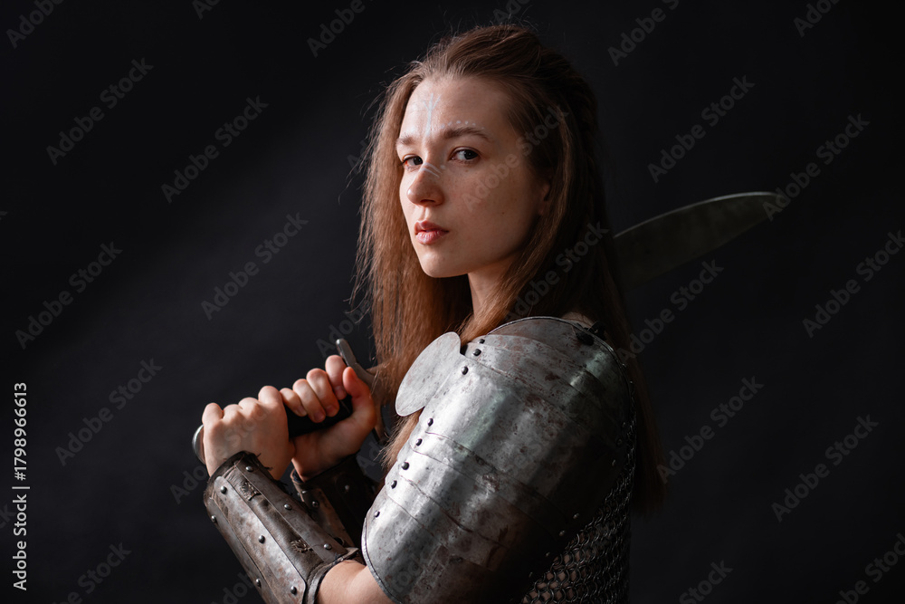 Naklejka premium Portrait of a young woman, fantasy warrior in armor with a sword in her hands isolated on a dark background