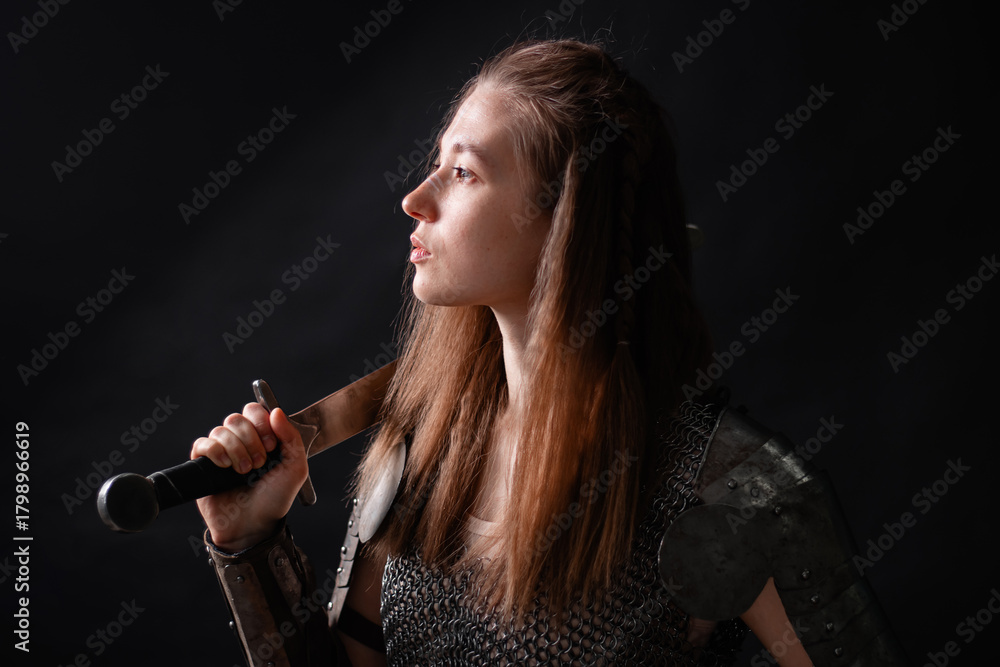 Naklejka premium Portrait of a young woman, fantasy warrior in armor with a sword in her hands isolated on a dark background
