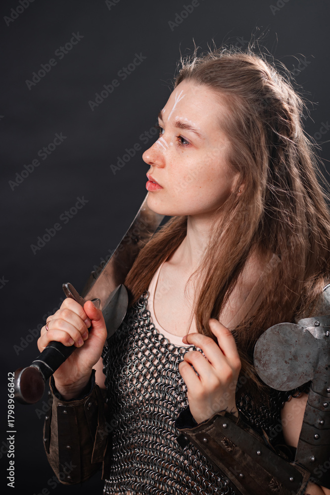 Naklejka premium Portrait of a young woman, fantasy warrior in armor with a sword in her hands isolated on a dark background