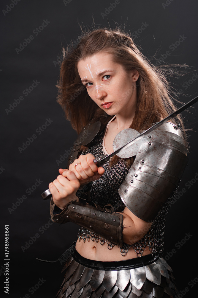 Naklejka premium Portrait of a young woman, fantasy warrior in armor with a sword in her hands isolated on a dark background