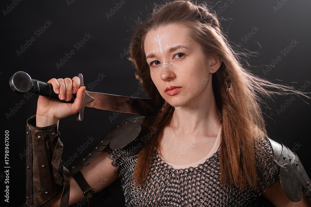 Naklejka premium Portrait of a young woman, fantasy warrior in armor with a sword in her hands isolated on a dark background