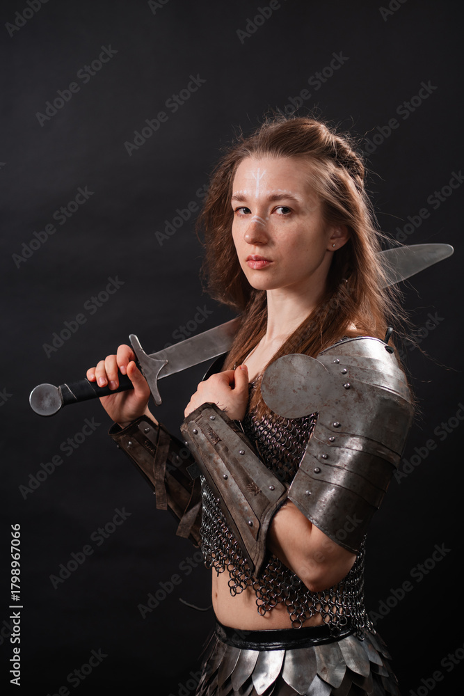 Naklejka premium Portrait of a young woman, fantasy warrior in armor with a sword in her hands isolated on a dark background