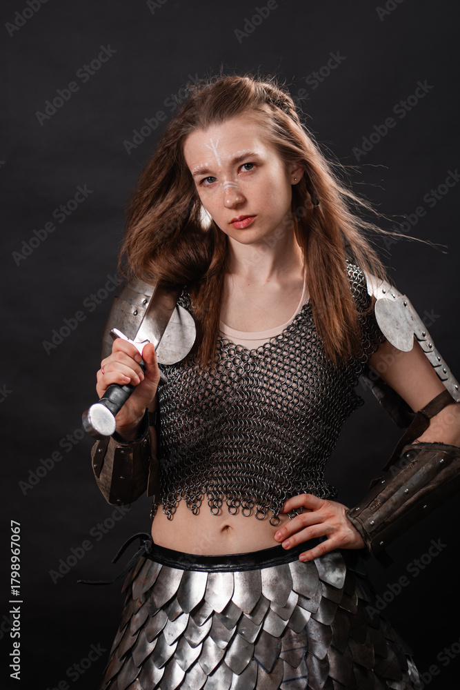 Naklejka premium Portrait of a young woman, fantasy warrior in armor with a sword in her hands isolated on a dark background
