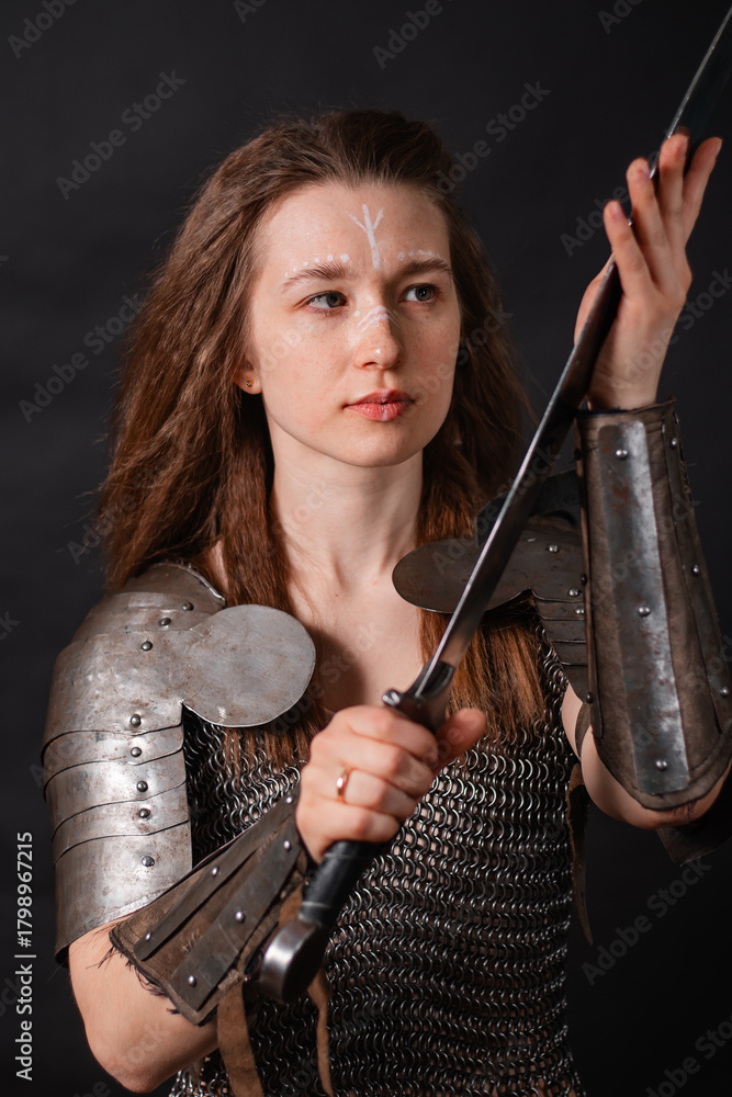Naklejka premium Portrait of a young woman, fantasy warrior in armor with a sword in her hands isolated on a dark background