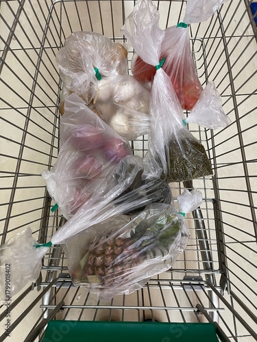 Fotografía A top-down view of a supermarket shopping cart filled with fresh produce packed in plastic bags for grocery retail