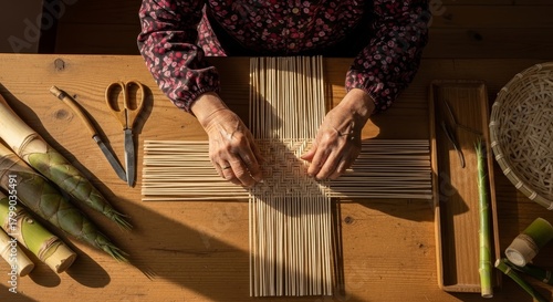 Elderly hands weaving traditional bamboo basket using natural reed strips on wooden workshop table with crafting tools