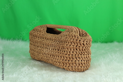 Crocheted cream bag on a white fluffy blanket in front of a green background.